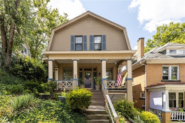 view of front of house featuring covered porch, stairway, and a gambrel roof