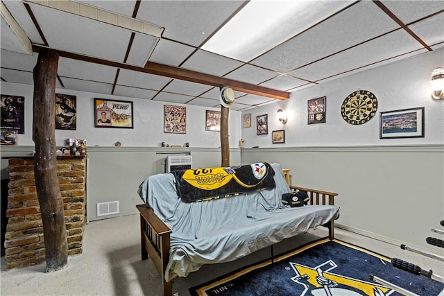 bedroom with a wainscoted wall, visible vents, and a drop ceiling