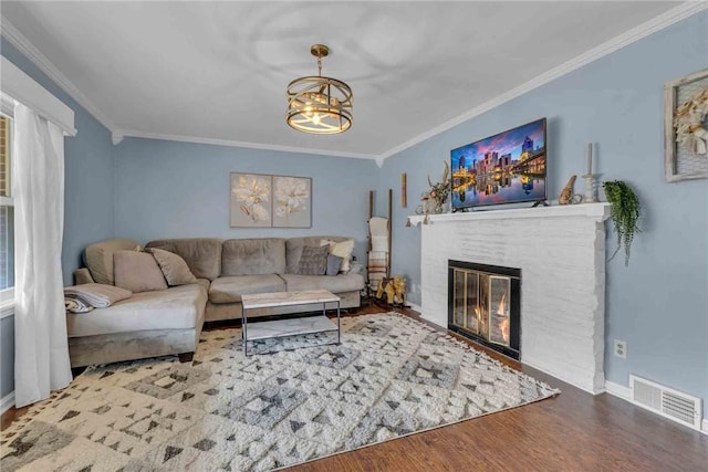 living room with visible vents, ornamental molding, wood finished floors, an inviting chandelier, and a brick fireplace