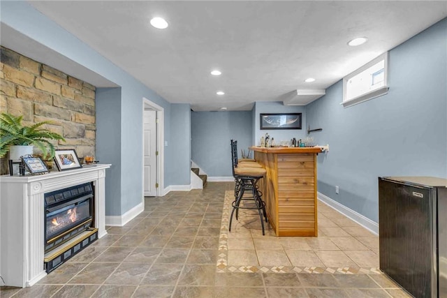 bar featuring recessed lighting, baseboards, stairway, a bar, and a glass covered fireplace