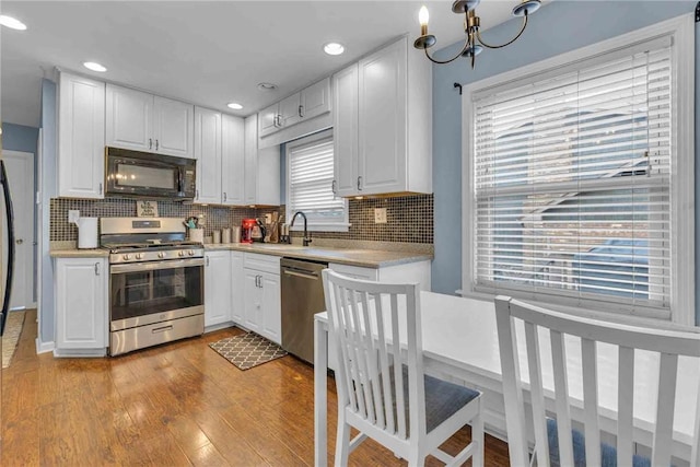 kitchen featuring light wood-style flooring, white cabinets, light countertops, appliances with stainless steel finishes, and decorative backsplash