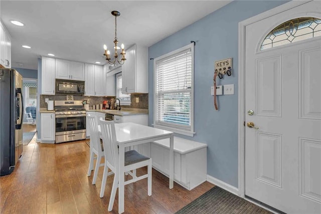 kitchen featuring a sink, light wood-style floors, white cabinets, black appliances, and tasteful backsplash