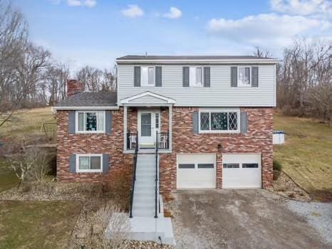 view of front facade featuring brick siding, driveway, a chimney, and an attached garage