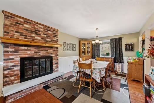 dining room with a brick fireplace, a wainscoted wall, a notable chandelier, and wood finished floors