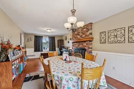 dining area featuring a wainscoted wall, a fireplace, wood finished floors, and an inviting chandelier