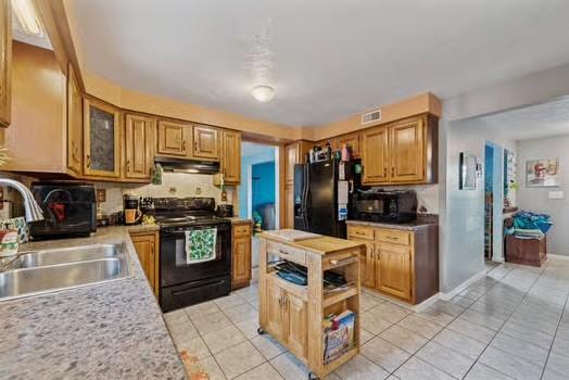 kitchen with visible vents, under cabinet range hood, light countertops, black appliances, and a sink