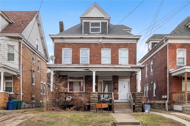 traditional style home featuring covered porch, a shingled roof, a front yard, and brick siding