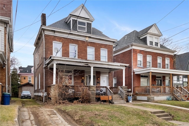 american foursquare style home featuring covered porch, brick siding, and a front yard