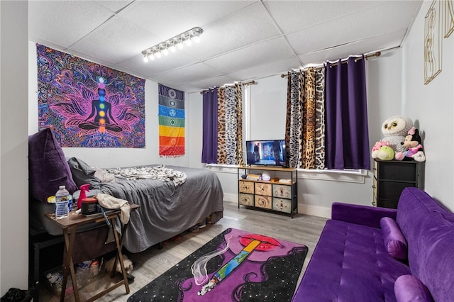 bedroom with a drop ceiling, wood finished floors, and baseboards