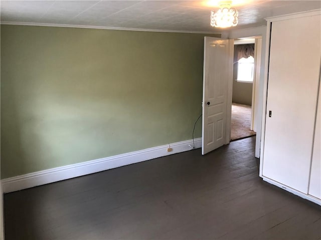 empty room with ornamental molding, dark wood finished floors, and baseboards