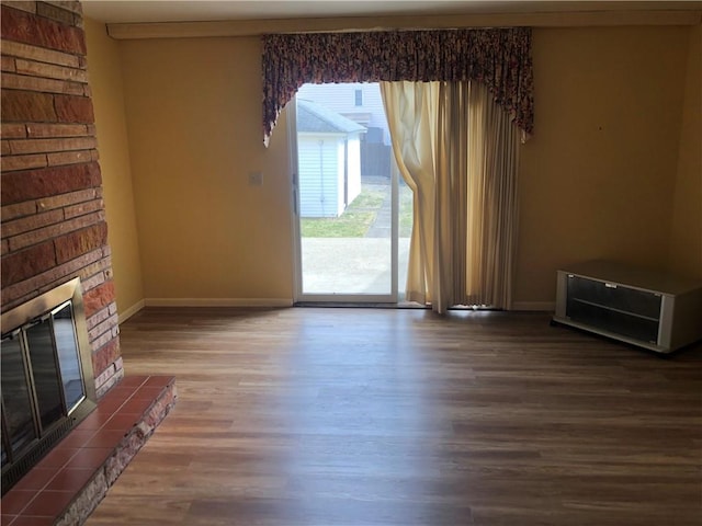 unfurnished living room featuring a tile fireplace, baseboards, and wood finished floors