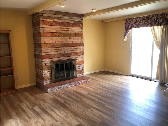 unfurnished living room featuring a fireplace, wood finished floors, beam ceiling, and baseboards