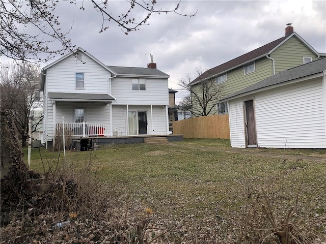 rear view of property with a yard, fence, and a chimney