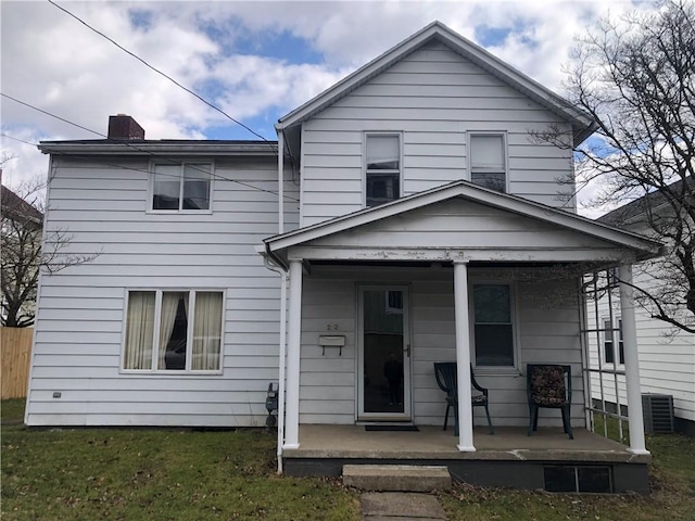 view of front facade with a porch, a front yard, fence, and a chimney