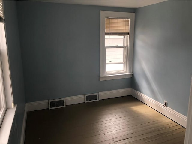 empty room with wood-type flooring, visible vents, and baseboards