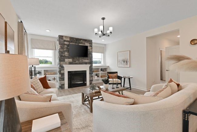 living room with a chandelier, a stone fireplace, light wood finished floors, and baseboards