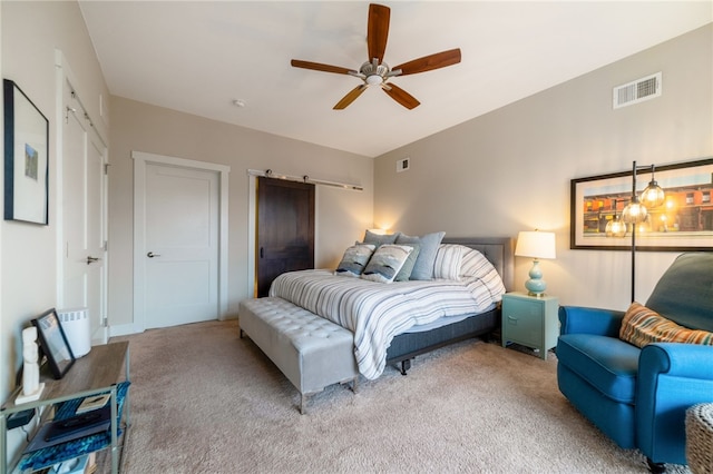 carpeted bedroom featuring a ceiling fan, visible vents, and a barn door