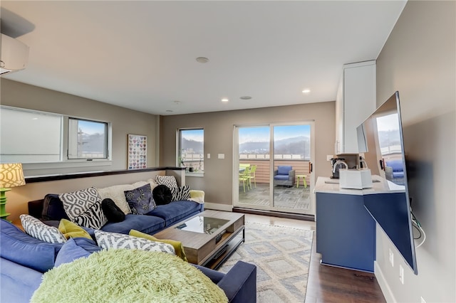 living room featuring a wall unit AC, baseboards, wood finished floors, and recessed lighting