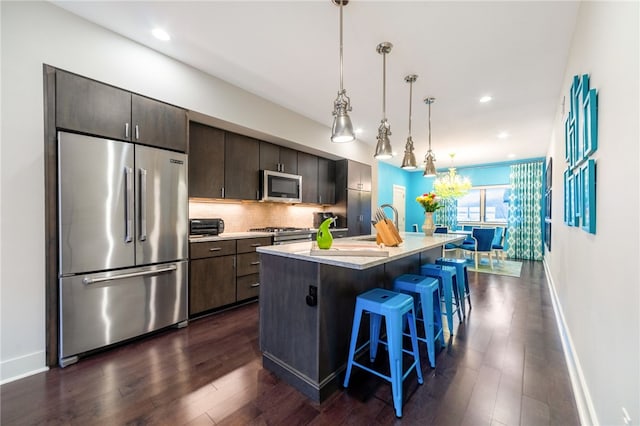 kitchen featuring a breakfast bar area, light countertops, appliances with stainless steel finishes, tasteful backsplash, and an island with sink