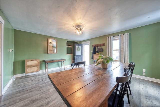 dining space featuring baseboards, arched walkways, and wood finished floors