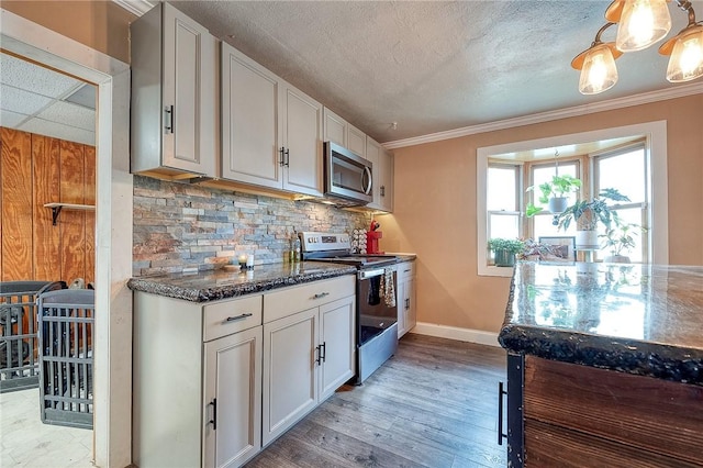 kitchen with stainless steel appliances, decorative backsplash, ornamental molding, dark stone countertops, and baseboards