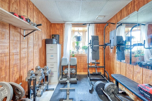 exercise room featuring a paneled ceiling and wooden walls