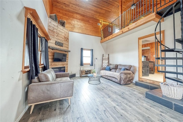 living area with a large fireplace, baseboards, a towering ceiling, wood ceiling, and wood finished floors