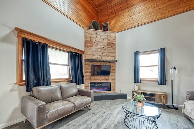 living area featuring high vaulted ceiling, baseboards, a tiled fireplace, and wood finished floors