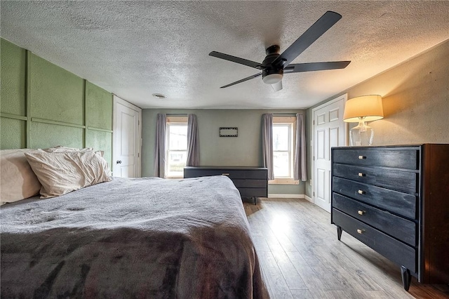 bedroom with a ceiling fan, a textured ceiling, baseboards, and wood finished floors