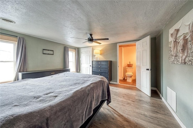 bedroom featuring connected bathroom, wood finished floors, visible vents, and baseboards