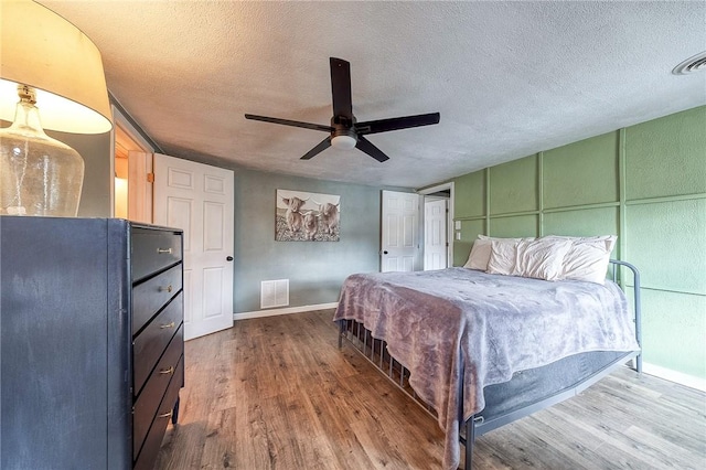 bedroom featuring a textured ceiling, wood finished floors, visible vents, and baseboards