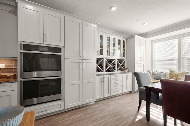 kitchen featuring tasteful backsplash, double oven, glass insert cabinets, white cabinetry, and light wood-type flooring