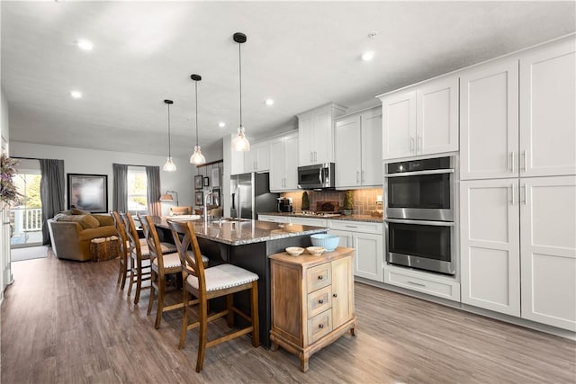 kitchen featuring stainless steel appliances, decorative backsplash, a sink, wood finished floors, and a kitchen bar