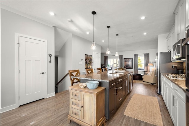 kitchen with stainless steel appliances, wood finished floors, a sink, open floor plan, and a center island with sink