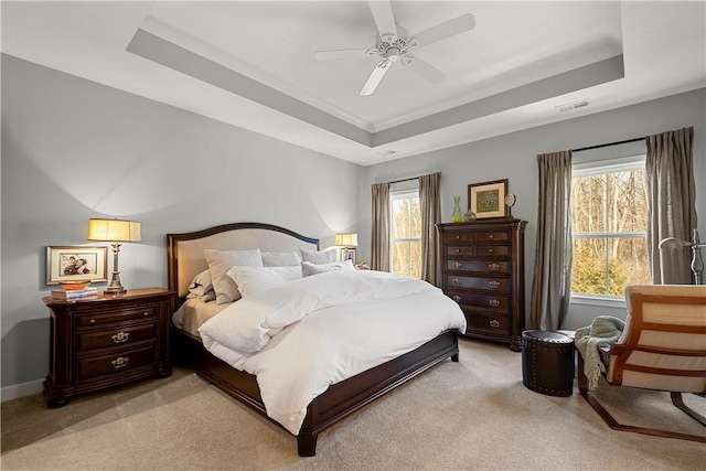 bedroom with light colored carpet, a raised ceiling, visible vents, and ceiling fan