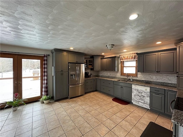 kitchen featuring white dishwasher, gray cabinetry, decorative backsplash, a sink, and stainless steel refrigerator with ice dispenser