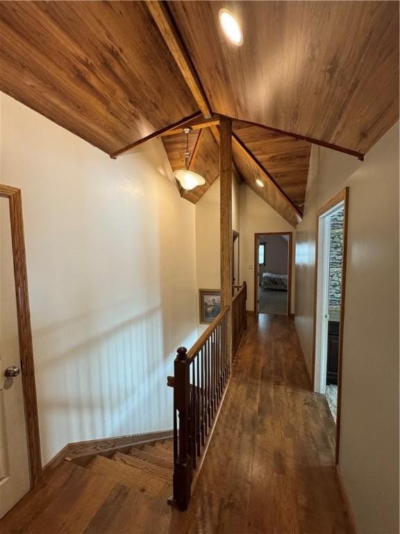 corridor with an upstairs landing, lofted ceiling with beams, wood finished floors, wooden ceiling, and baseboards