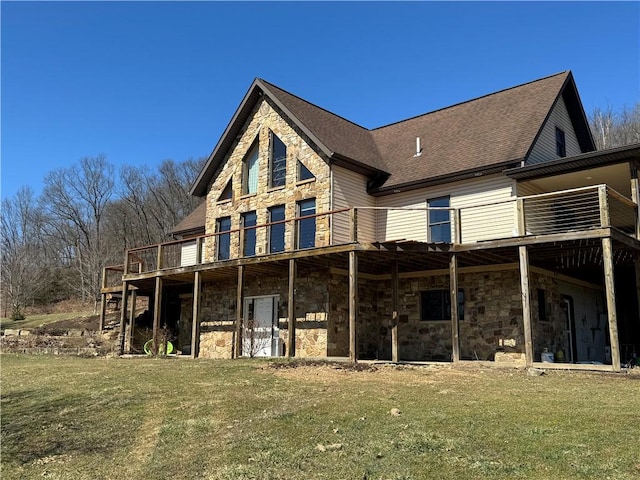 back of property with a shingled roof, a lawn, stone siding, and a wooden deck