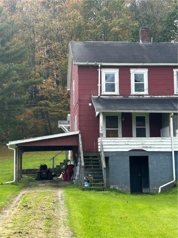 view of front of house featuring stairs, driveway, a carport, a chimney, and a front yard