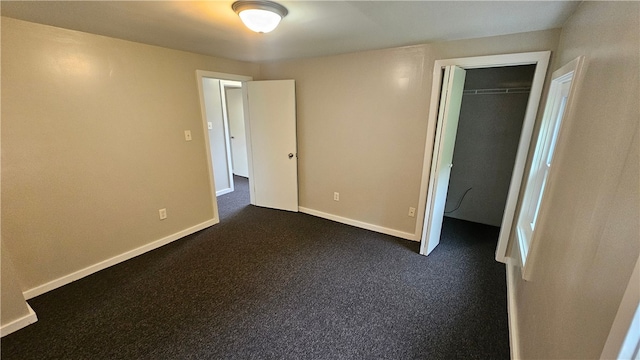 unfurnished bedroom with baseboards, dark carpet, a walk in closet, and a closet