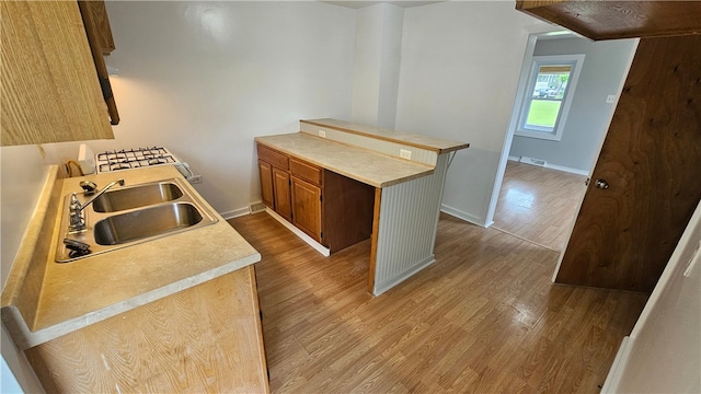 kitchen with a peninsula, wood finished floors, a sink, baseboards, and light countertops