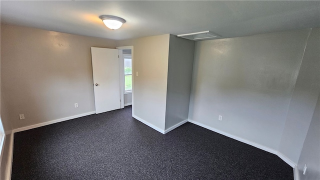 empty room with dark carpet, attic access, and baseboards