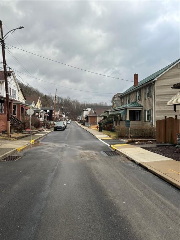 view of asphalt road featuring a residential view, sidewalks, curbs, and street lighting