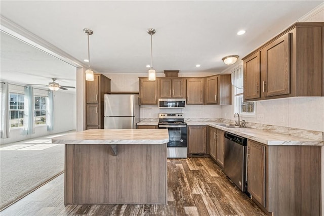 kitchen with appliances with stainless steel finishes, hanging light fixtures, light countertops, dark carpet, and a sink