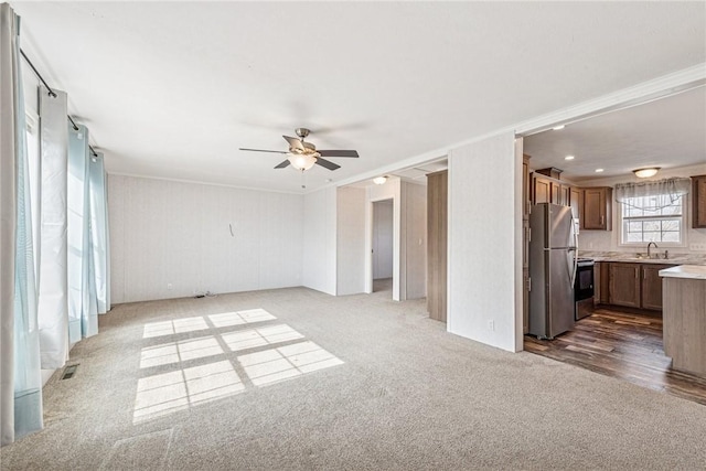 unfurnished living room with carpet floors, a sink, visible vents, a ceiling fan, and ornamental molding