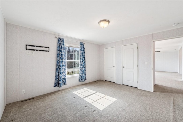 unfurnished bedroom featuring carpet floors, visible vents, and multiple closets