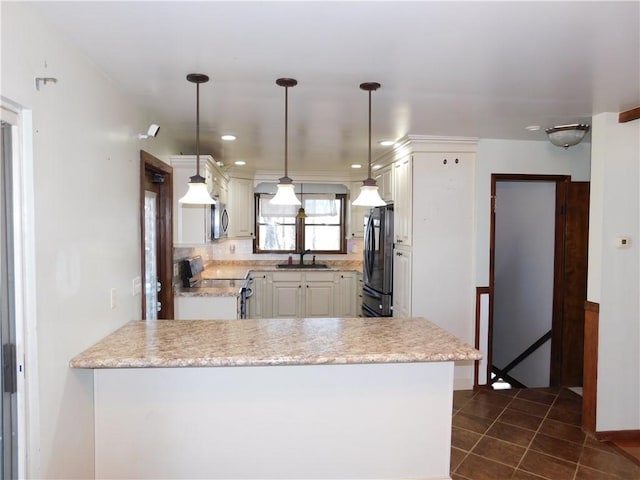 kitchen featuring a peninsula, stainless steel appliances, light countertops, dark tile patterned floors, and a sink