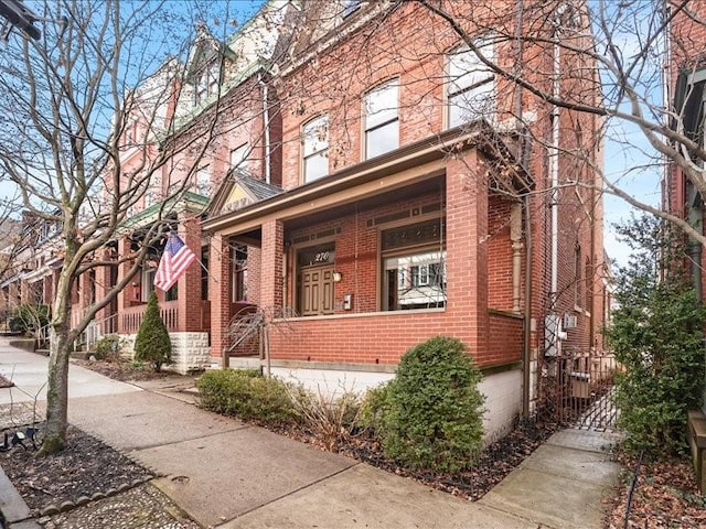 view of front of house with covered porch, brick siding, and a gate