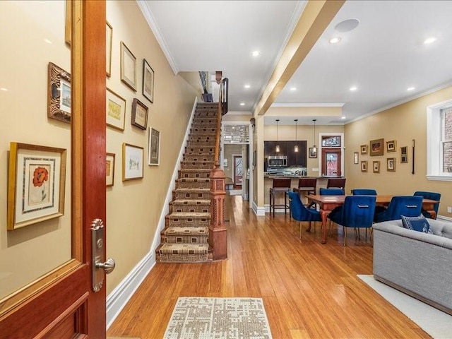 foyer featuring baseboards, ornamental molding, stairway, and light wood-style floors