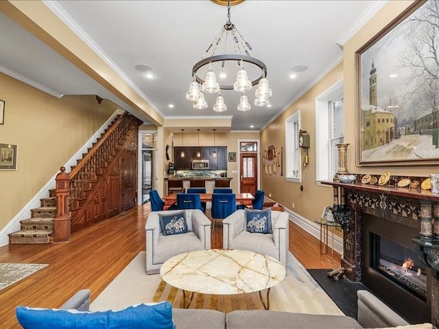 living room with a fireplace with flush hearth, ornamental molding, wood finished floors, an inviting chandelier, and stairs